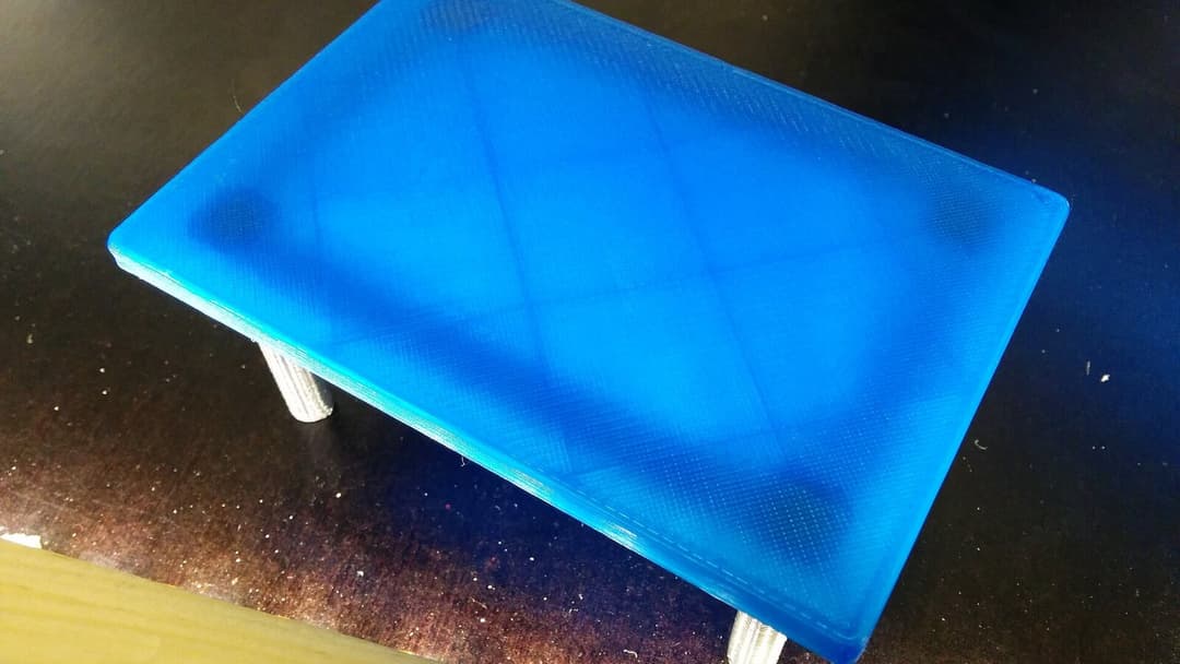 A small blue 3D-printed object on a dark surface, its top showing a fine grid of printed layer lines.