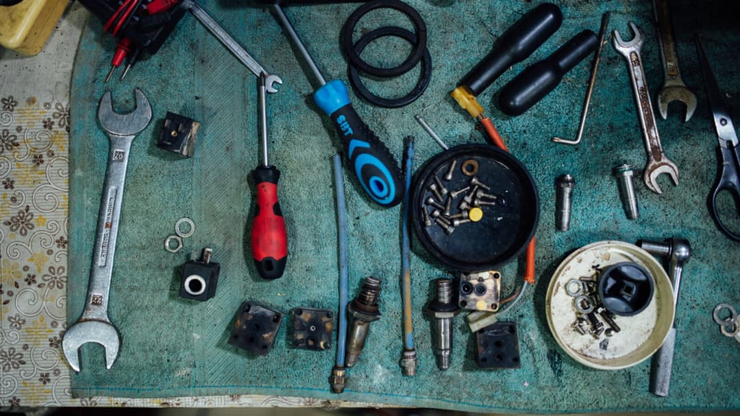 Two screwdrivers, one red and one blue, spanners, a ratchet handle, a pair of meter probes and small solenoid parts laid out on a cloth on a workbench.