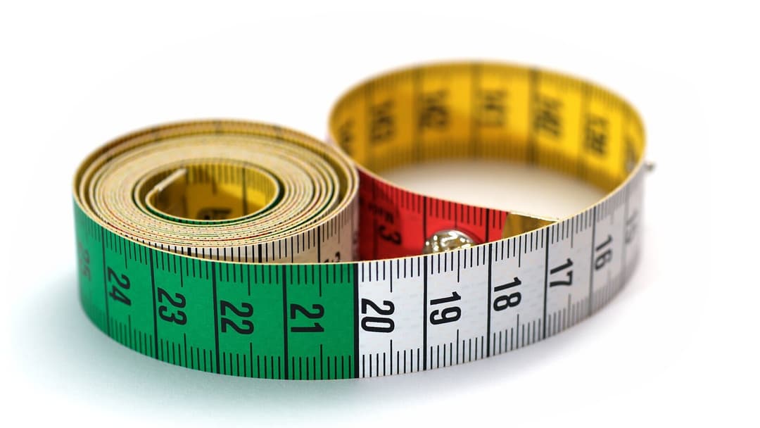 A colourful cloth tape measure coiled into a loop on a white surface, its centimetre markings showing.