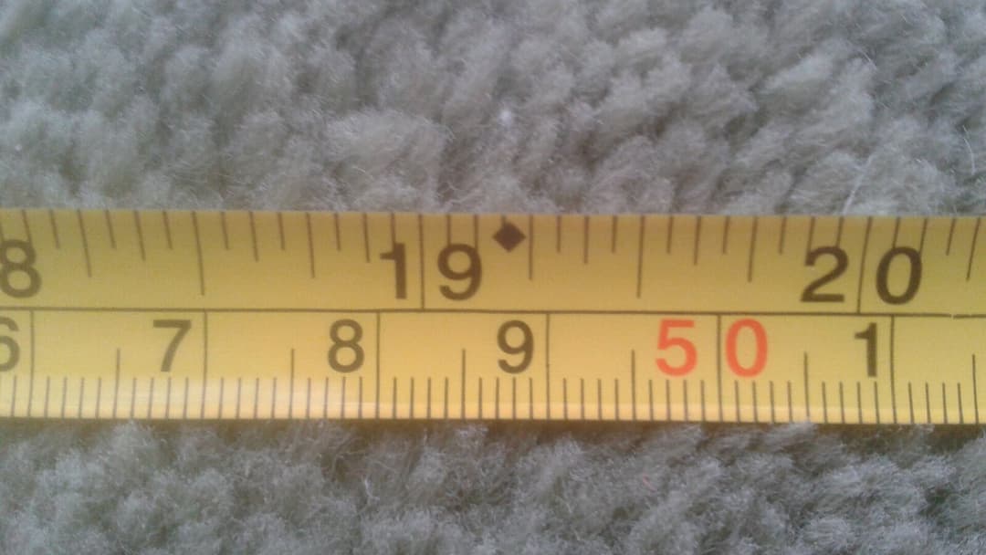 A close-up of a yellow measuring tape laid on grey carpet, its dual centimetre and inch scale in sharp focus around the fifty-centimetre mark.