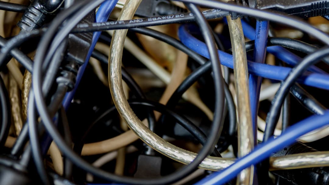 A close-up of a dense tangle of black, blue and pale data and power cables knotted together.