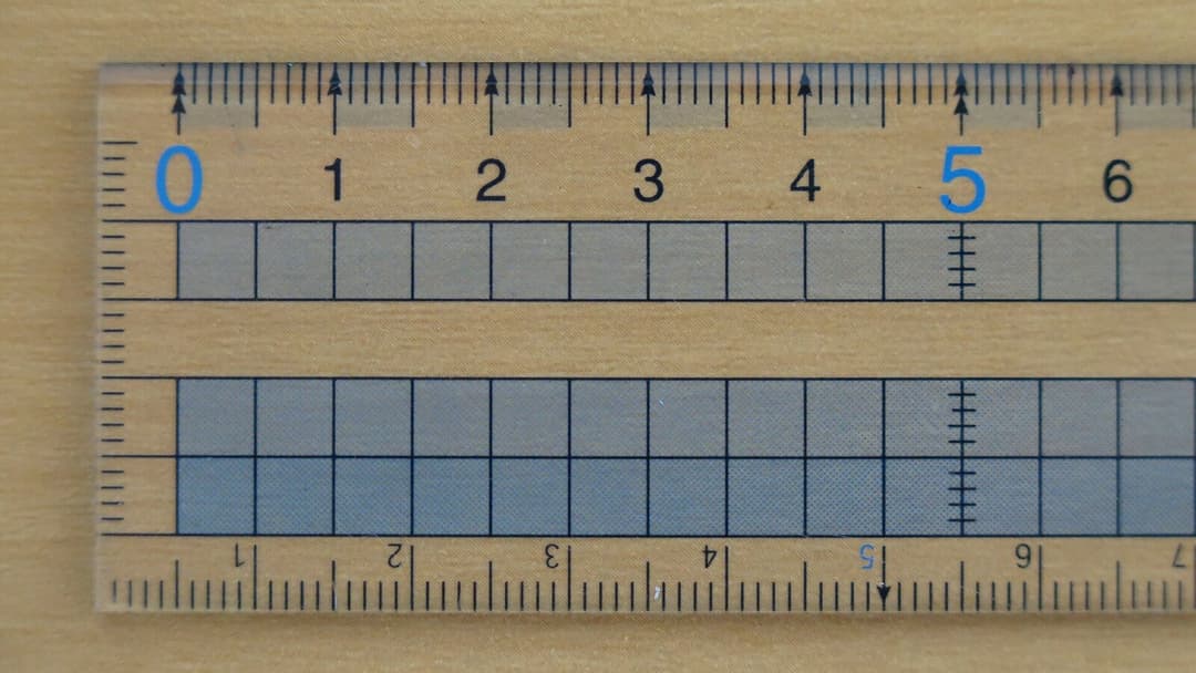 A transparent ruler with centimetre markings from zero to six resting on a light wooden table top.