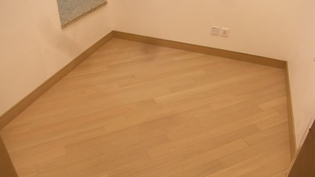 An empty compact bedroom with pale wood flooring, plain cream walls and a three-pin power socket above the skirting board.