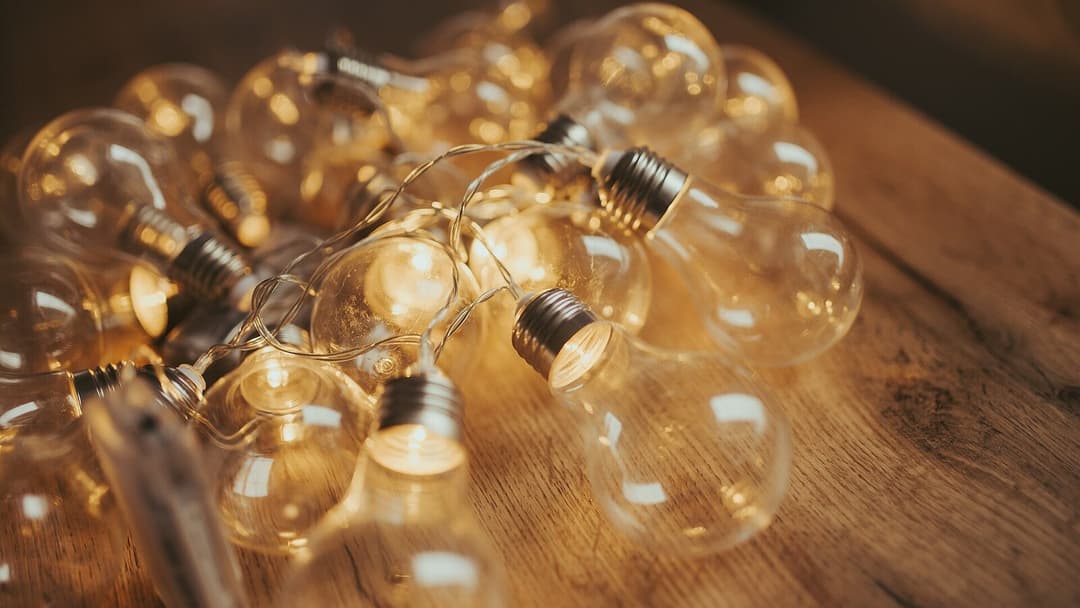 A cluster of clear glass bulbs with silver metal screw bases, linked by a thin wire, glow warm on a wooden surface.