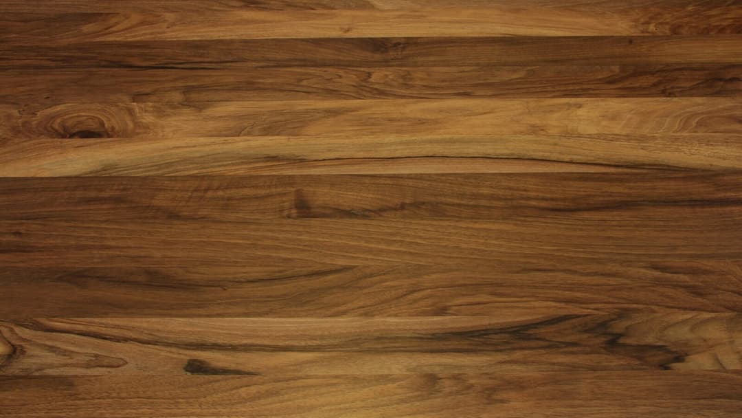 Close-up of a solid European walnut wood surface, several planks joined side by side showing warm brown grain, darker streaks and a small knot.
